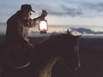 A cowboy on a horse holding a lamp