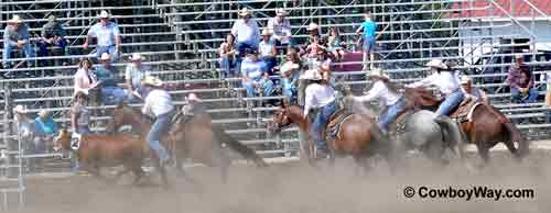 Four cowgirls ride hard to turn their calf up the fence