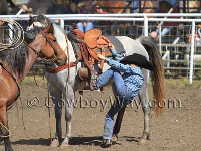 A young girl stetches a long way to mount a horse