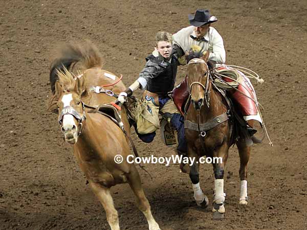 A young bareback bronc rider has trouble getting off his bronc