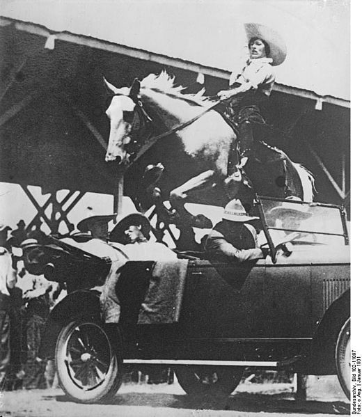 Unknown cowgirl jumping a horse over a car