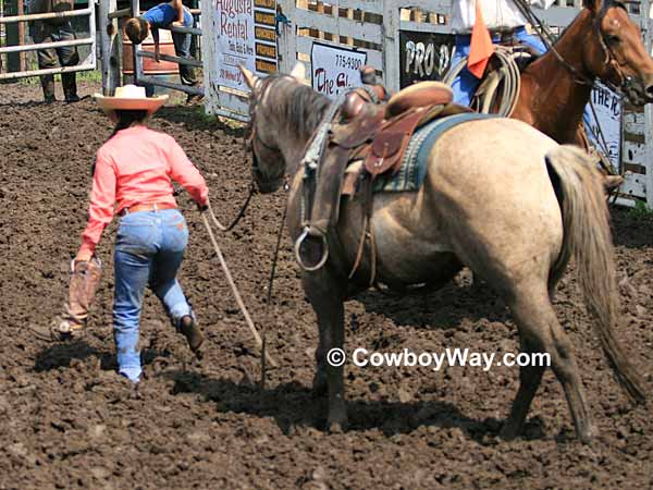 A cowgirl carries her boot that was sucked off in the mud