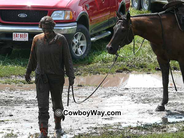 A lone cowgirl covered in mud and her horse