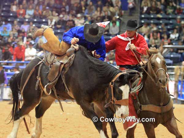 A pickup man helps a bronc rider