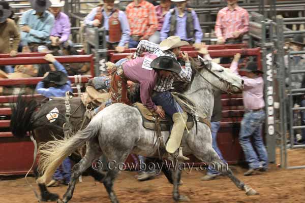 A pickup man helps a saddle bronc rider off his bronc
